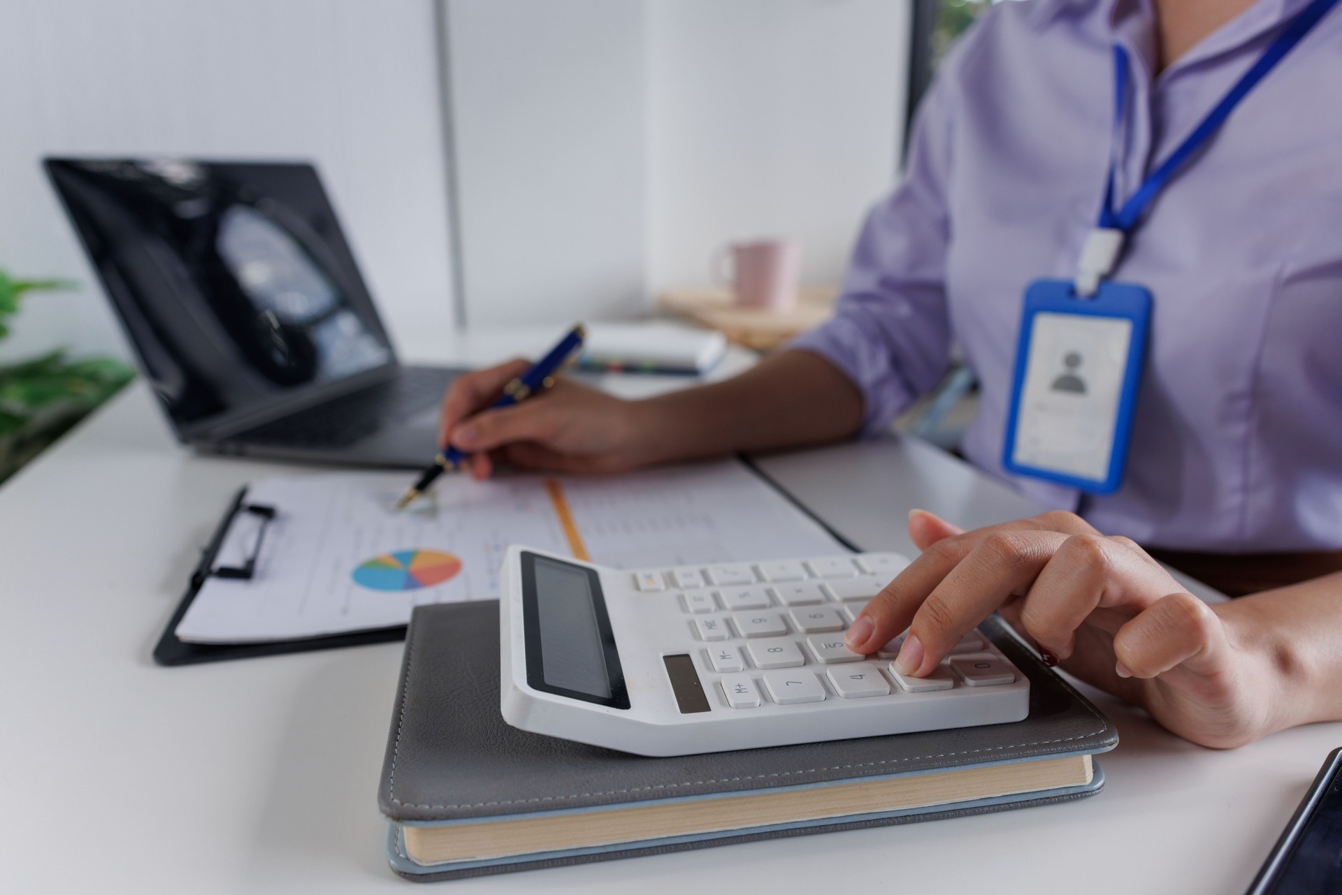 Close up of business woman or accountant hand holding pen working on calculator to calculate business data, accountancy document and laptop computer at office, business concept Close up of business woman or accountant hand holding pen working on calculator to calculate business data, accountancy document and laptop computer at office, business concept